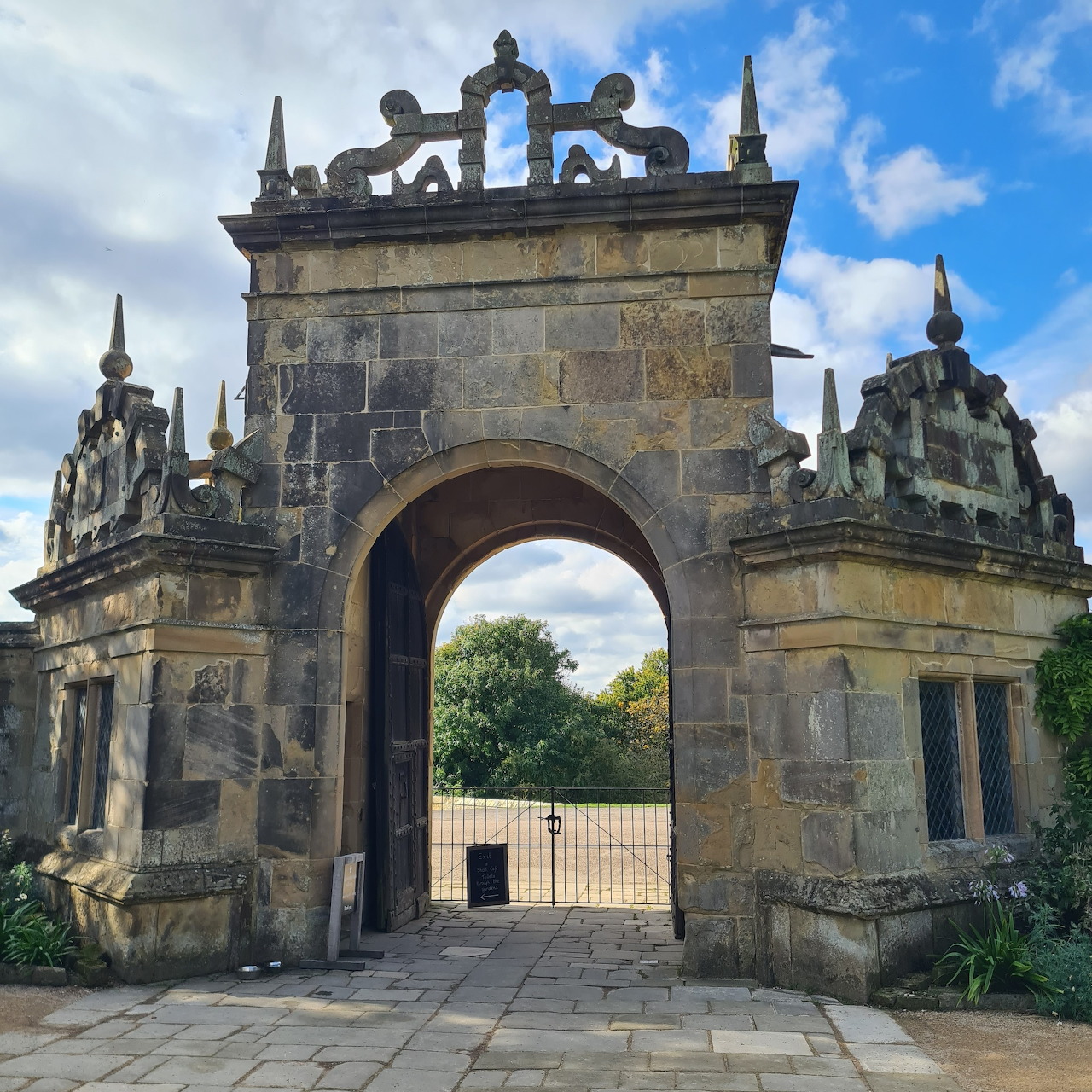 Historic stone archway entrance with ornate spires and a cloudy sky
