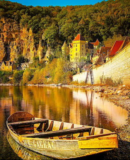 Wooden boats on river by French village with cliff backdrop