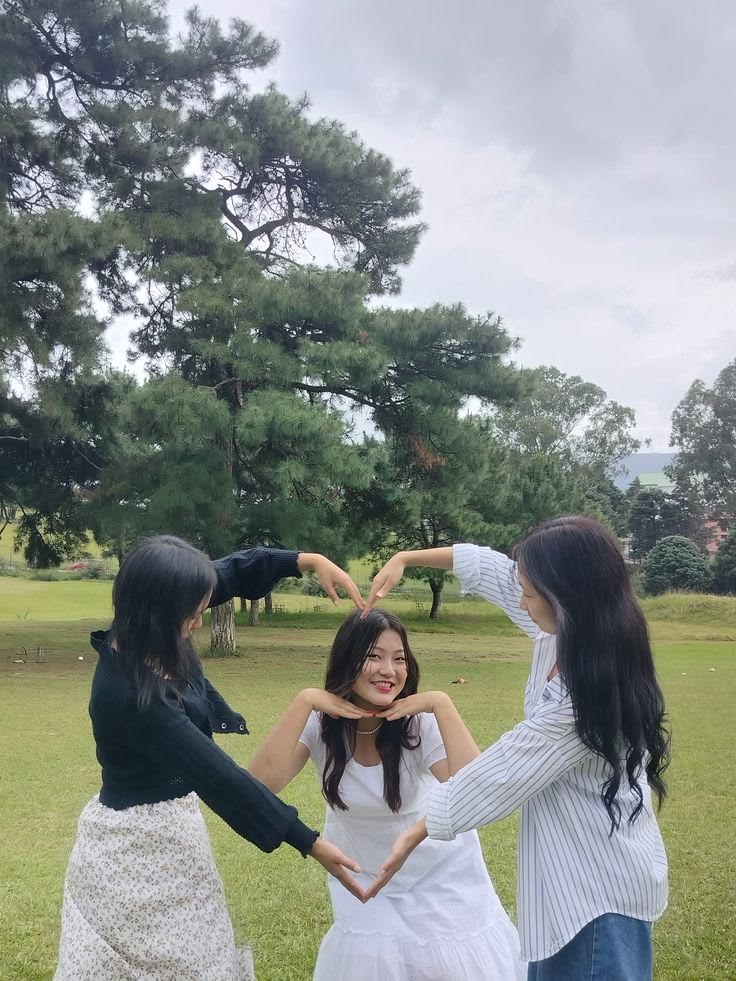 Three women on a lawn making a heart shape with their arms outdoors