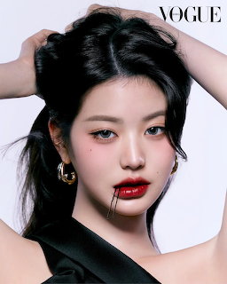 Studio portrait of Wonyoung with dark hair, red lipstick, gold hoop earrings, and a black draped top