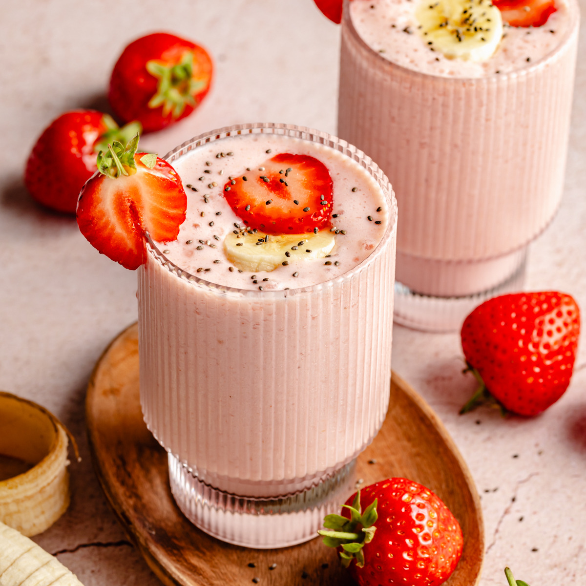Two glasses of strawberry smoothie topped with fruit, with fresh strawberries around them