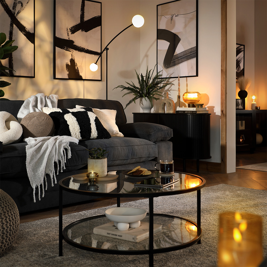 Modern living room with gray sofa, round glass coffee table, wall art, and double bulb arc lamp