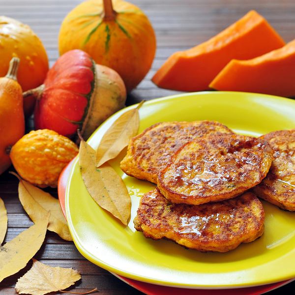 Stack of golden pumpkin pancakes on green plate with decorative pumpkins and autumn vegetables on wooden table