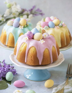 Three pastel bundt cakes with icing and candy eggs on cake stands with flowers