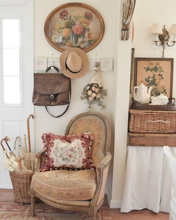 Vintage entryway with antique chair, straw hat, leather bag, wicker baskets, and floral wall art