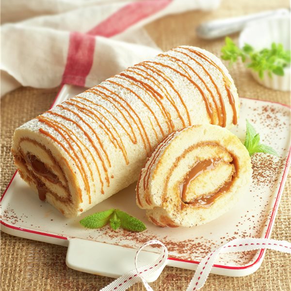 Caramel-drizzled Swiss roll cake with one slice on a white plate