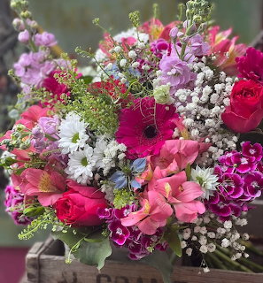 Colorful bouquet with pink gerberas, red roses, hydrangeas, baby's breath, and purple flowers in a wooden crate