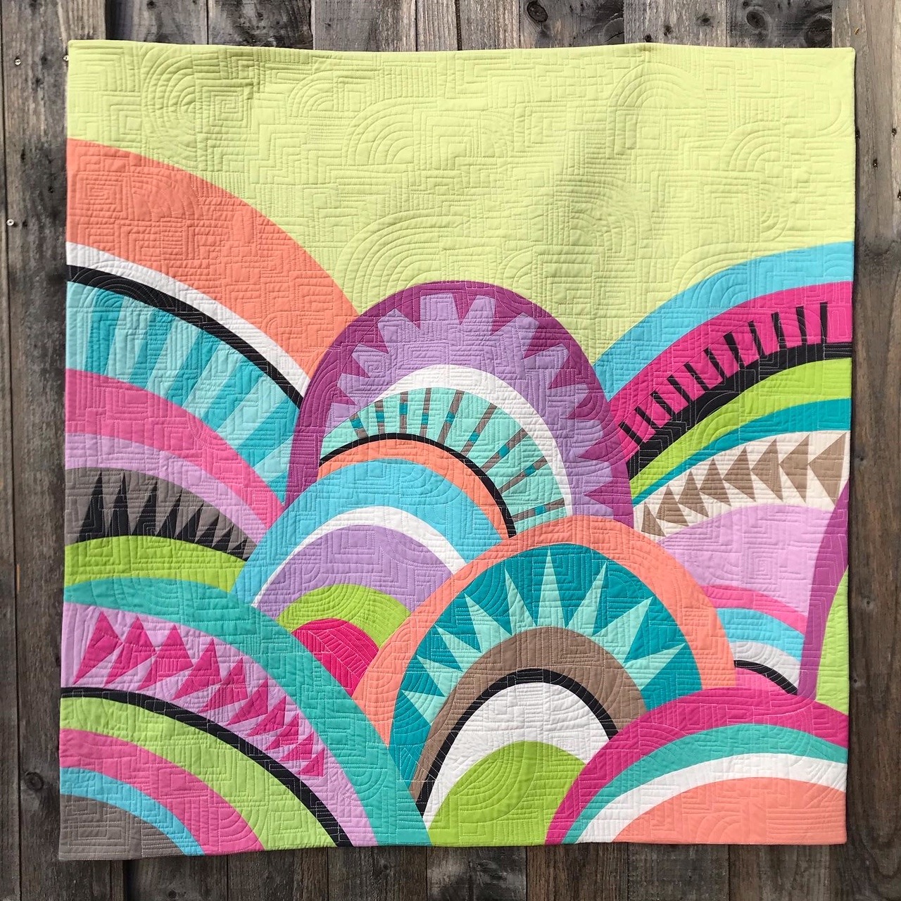 Colorful quilt with overlapping geometric fan patterns in pink, turquoise, yellow and coral on textured fabric