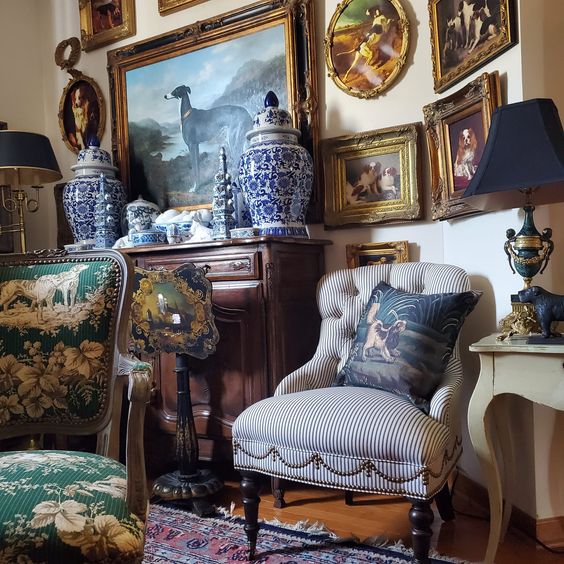 Vintage-style interior with striped armchair, framed paintings, porcelain vases, and wooden furniture