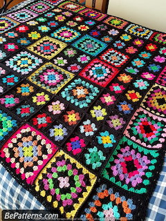 Multicolored granny square crochet blanket with black borders on checkered bed