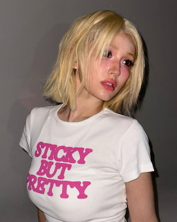 Portrait of woman with blonde bob haircut in white graphic tee on gray background