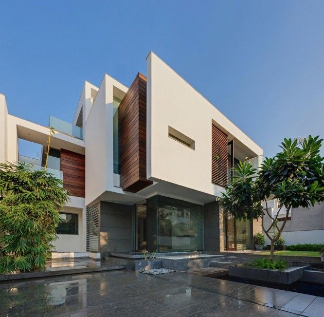 Modern white two-story house with geometric shapes, wood panels, and tropical landscaping