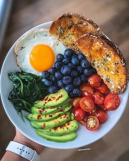Overhead view of a breakfast bowl with fried egg, blueberries, avocado, tomatoes, spinach, and toast