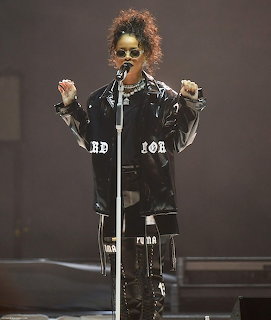 Female singer in black leather jacket and sunglasses performing on stage with microphone