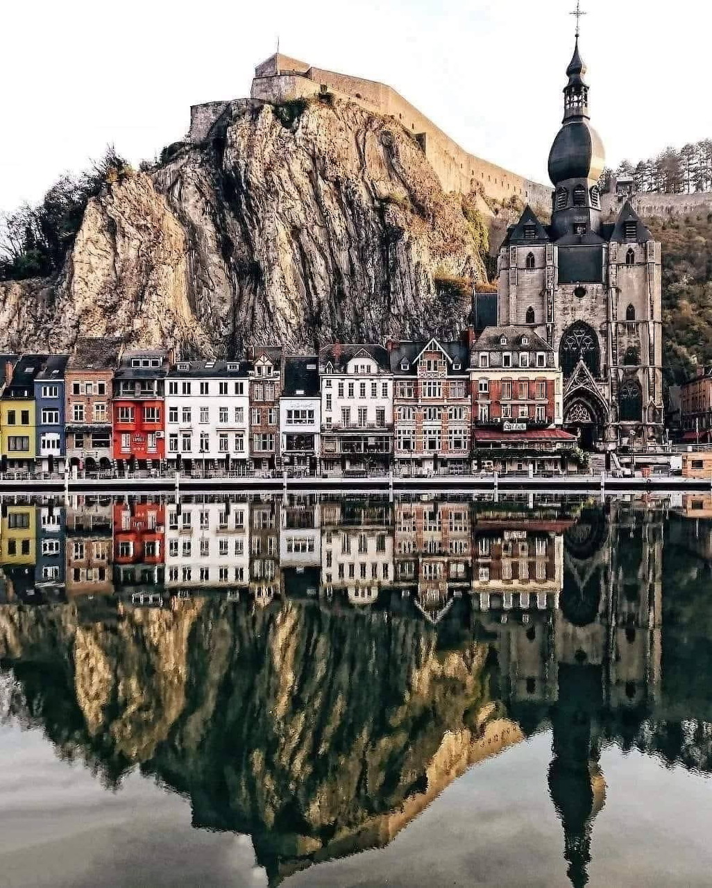 Colorful buildings and church of Dinant Belgium reflected in the Meuse River with cliff and citadel above