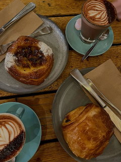 Flatlay of coffee cups with latte art and pastries on turquoise plates on wooden table