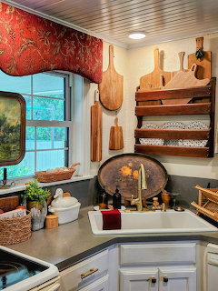 Cozy cottage kitchen with wooden cutting boards, white sink, red valance, and rustic decor