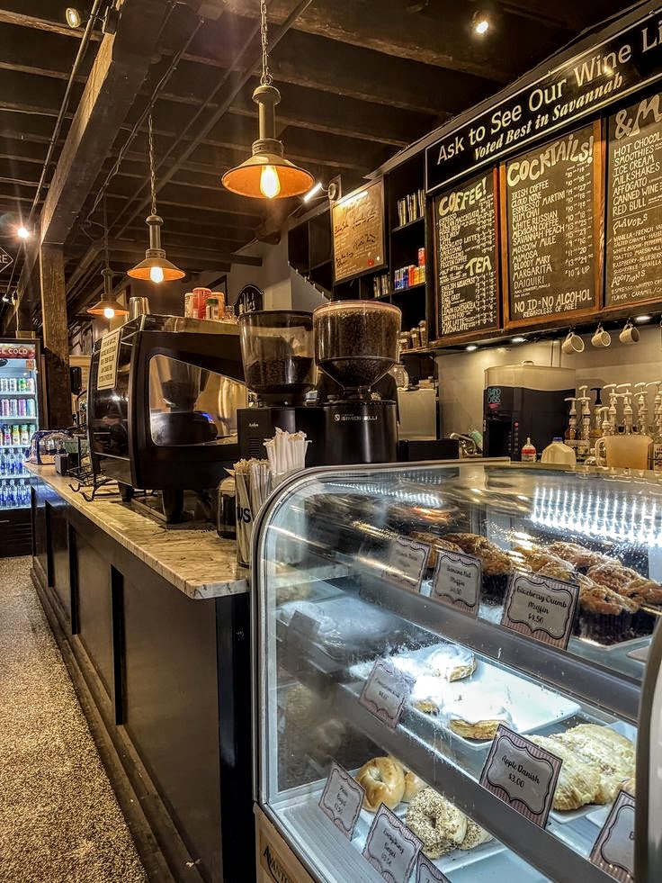 Coffee shop counter with glass pastry display case, espresso machines, and chalkboard menus on the wall