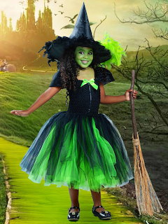 Child dressed as green witch with tutu, hat, face paint and broom in front of castle backdrop