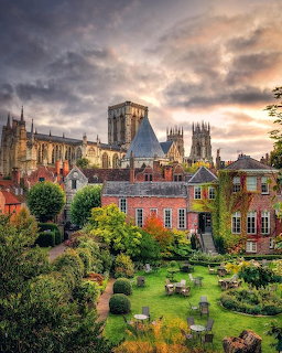 York Minster cathedral towering over a green garden and red-brick houses under a dramatic cloudy sky