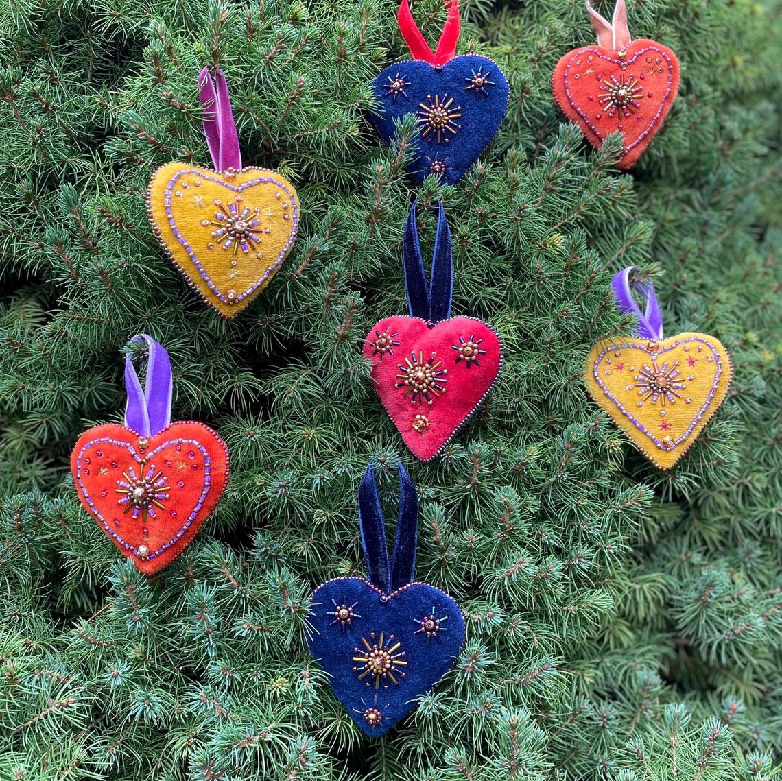 Colorful embroidered felt heart ornaments hanging on green evergreen branches