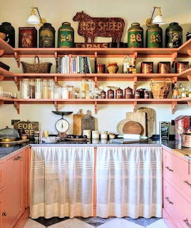 Vintage farmhouse kitchen with open shelves, antique canisters, cookbooks, and coral cabinets with curtain