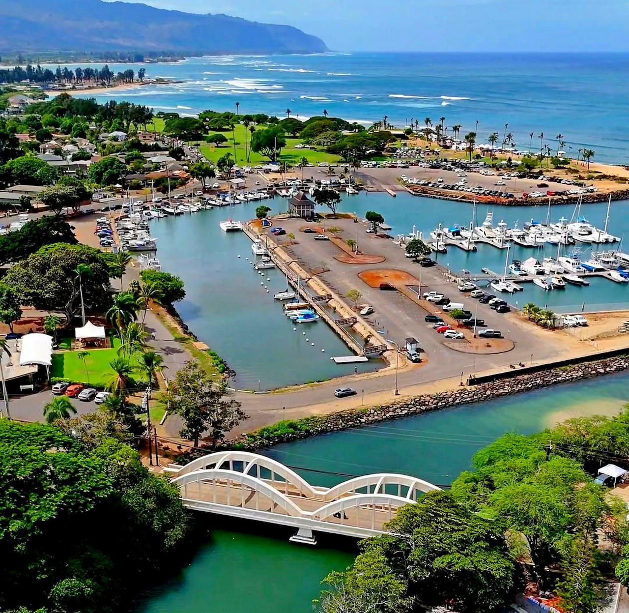 Aerial view of a Hawaii marina with boats, a white bridge, beach, and blue coastal water