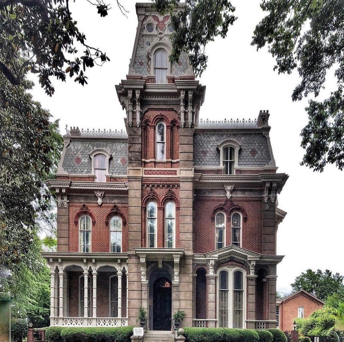 Historic Victorian brick mansion with a central tower and ornate facade framed by trees