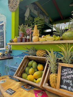 Tropical fruit market stand with pineapples, bananas, and fresh produce displayed in wooden crates under bright colored awning