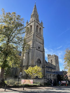 Gothic stone church with tall spire surrounded by green trees against a blue sky