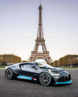Grey supercar with blue accents parked on a paved area with the Eiffel Tower in the background