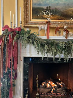 Christmas mantle with garland, stockings, candles, and framed landscape painting above a lit fireplace