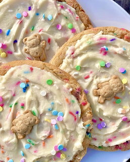 Round cookies with white frosting, rainbow sprinkles, and teddy bear graham crackers on top