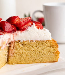 Slice of sponge cake topped with whipped cream and fresh strawberries on a white surface