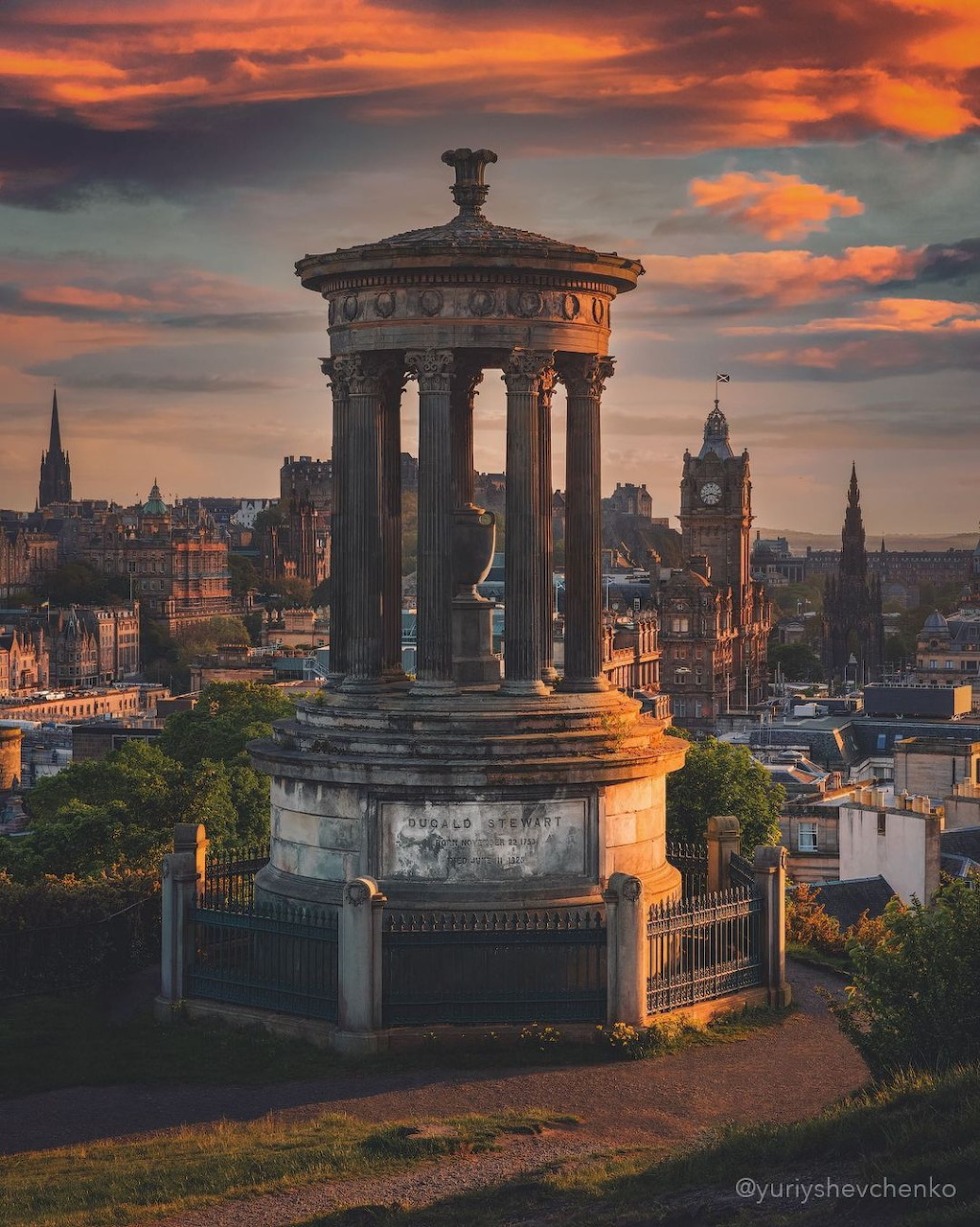 Stone monument with columns on hillside overlooking Edinburgh at sunset