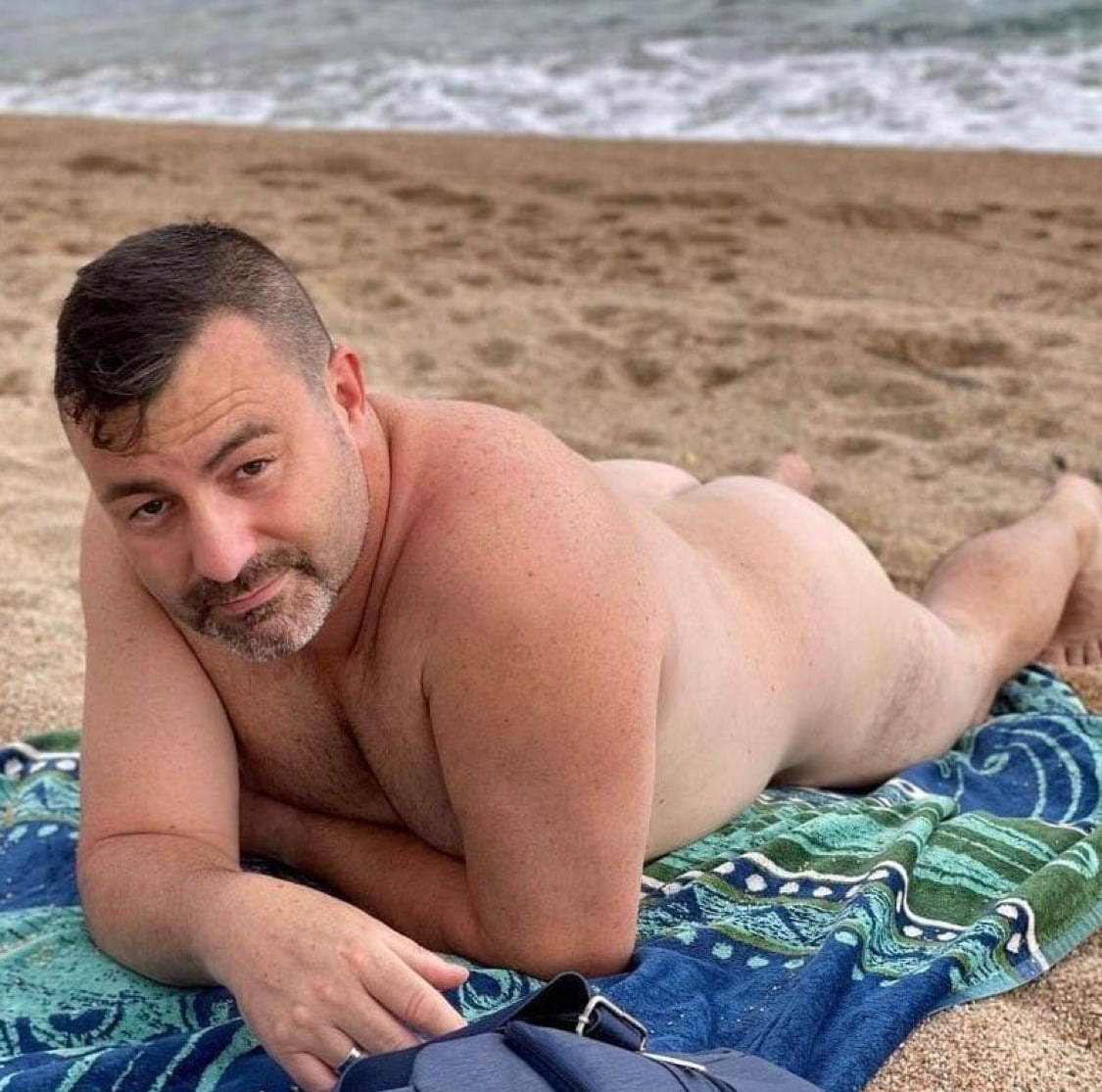 Shirtless man resting on patterned beach towel with ocean waves behind him