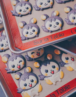 Purple bat-shaped macarons with smiling faces on red baking mats with orange candy pieces scattered around