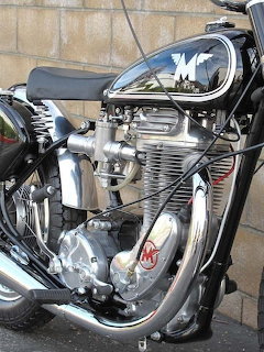 Vintage Matchless motorcycle engine with polished chrome cylinder head and exhaust pipes against stone wall background