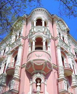 Ornate pink and white classical building facade with balconies and decorative stucco seen from below