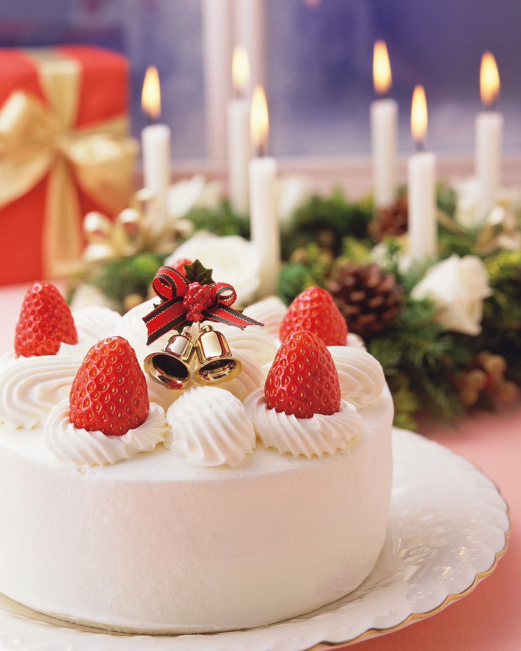 White Christmas cake with strawberries and cream in front of lit candles and festive decorations
