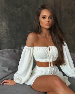 Woman with long brown hair in white off-shoulder top and shorts sitting on gray couch
