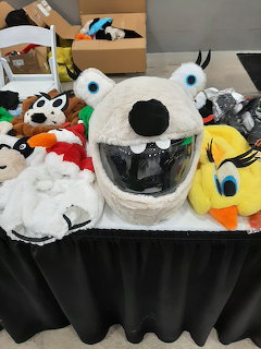 Novelty plush helmet covers shaped like cartoon characters displayed on a black tablecloth at a vendor booth
