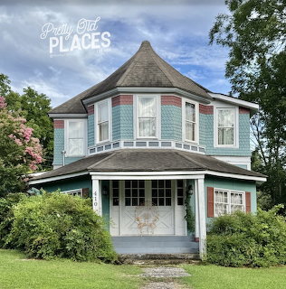 Blue Victorian-style house with porch, bushes, and trees