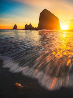 Sunset over sea stacks with waves washing onto a dark sandy beach