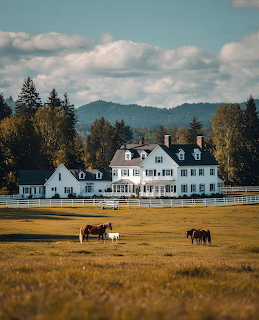 White farmhouse with horses grazing in front, mountains and trees behind under cloudy sky