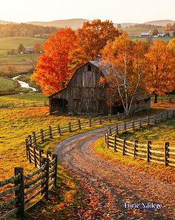 Old wooden barn with split-rail fence surrounded by colorful autumn trees and winding country road