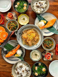 Overhead view of a Korean meal spread with rice bowls, stew, side dishes, and sliced oranges on a wooden table