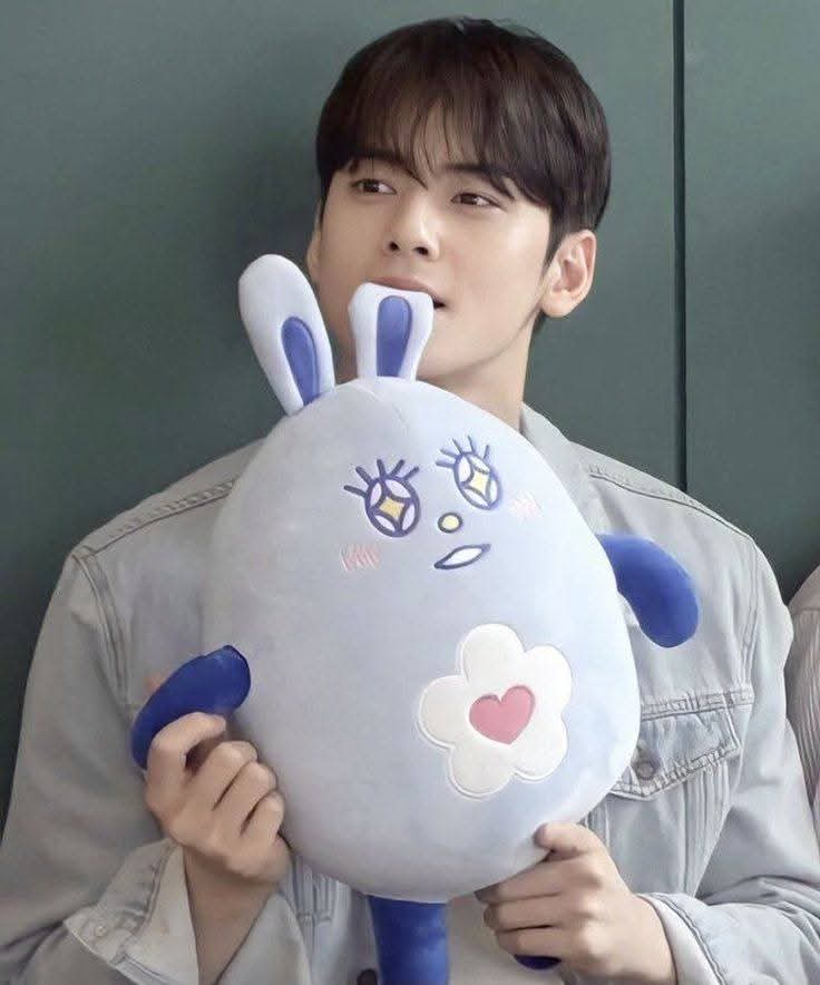 Young man holding a blue bunny plush toy indoors