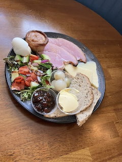 Ploughman's lunch platter with ham, cheese, bread, eggs, salad, and chutney on a dark plate