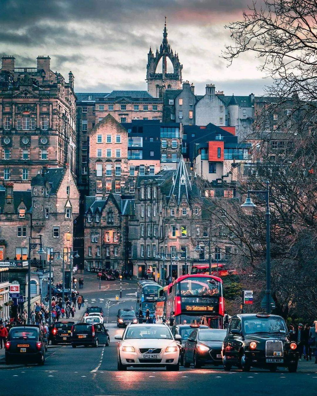Historic Edinburgh street with clock tower, traffic, and traditional Scottish buildings under moody sky